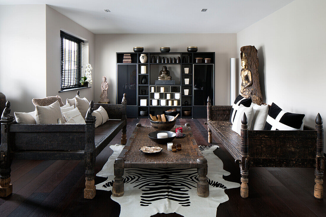 Pair of carved wooden daybeds with low wicker table in Zen styled London home,  England,  UK