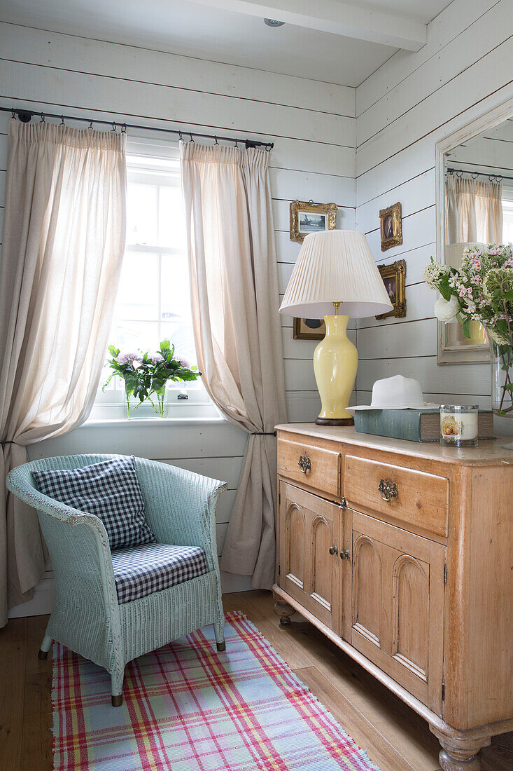 Painted wicker armchair with gingham cushions at sunlit window in Surrey home, England, UK