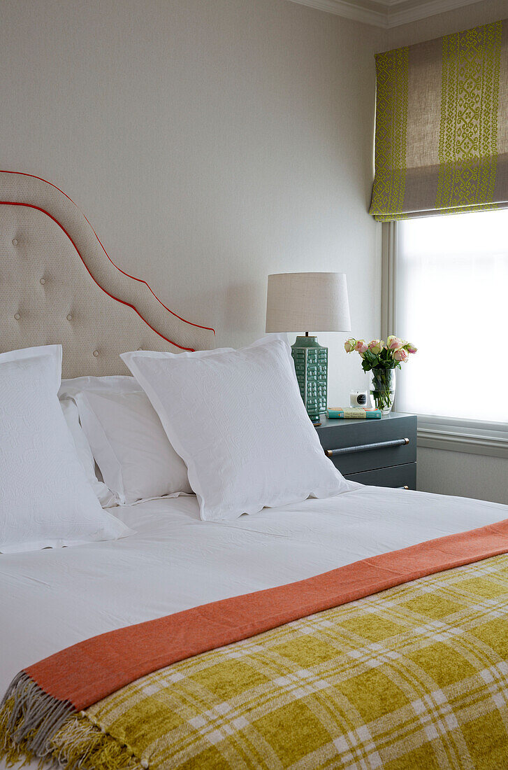 Checked yellow blanket on double bed with buttoned headboard at window in London home, England, UK