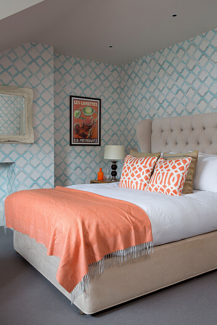 Leuchtend orangefarbener Bettbezug auf einem Doppelbett mit blau gemusterter Tapete in einem Haus in London, England, UK