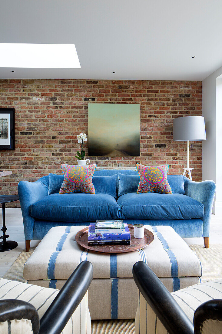 Bücher auf Ottomane mit blauem Zweisitzer-Sofa im Wohnzimmer eines Hauses in London, England, UK