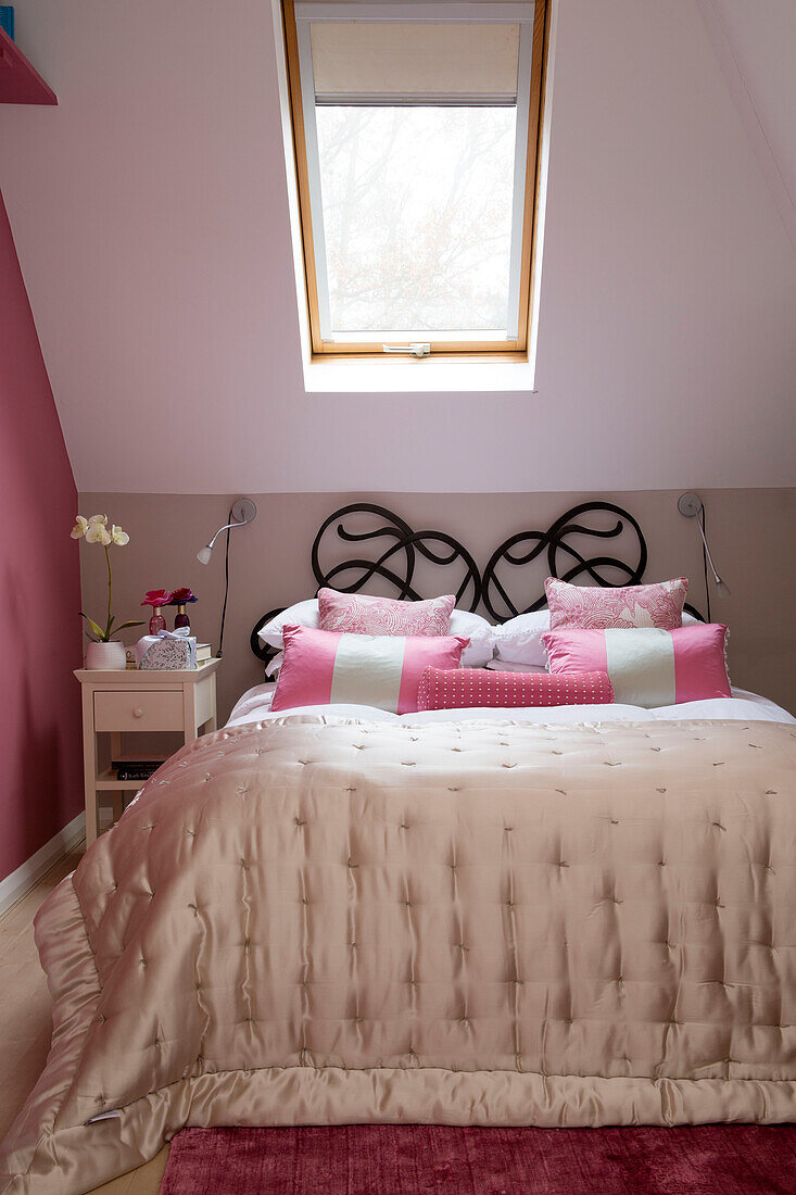 Cream quilt on double bed with wrought iron headboard below skylight attic window in Chobham home   Surrey   England   UK