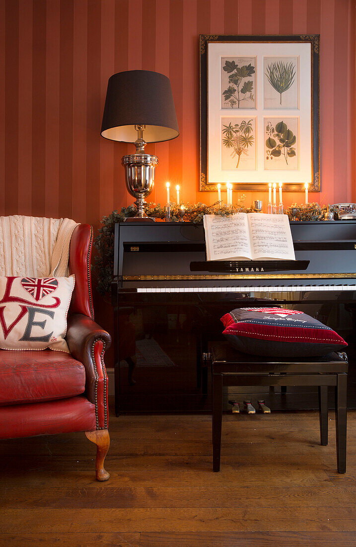 Red leather armchair beside piano with lit candles in Surrey home   England   UK