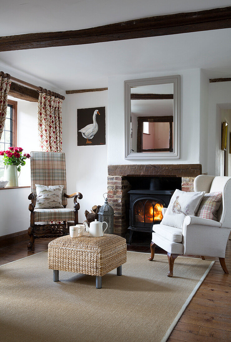 Wingback armchair with lit wood burning stove in Sussex farmhouse   England   UK