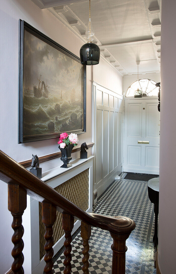 Polished wooden banister with framed artwork above radiator cover in chequered hallway of London townhouse   England   UK