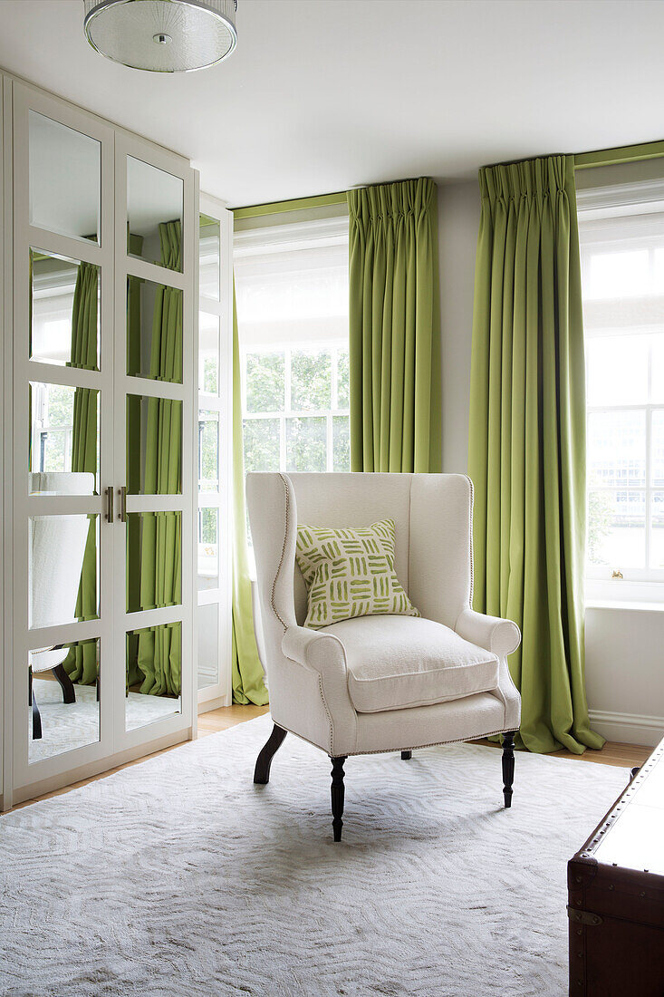 White armchair and mirrored wardrobe with lime green curtains in bedroom of London townhouse England UK