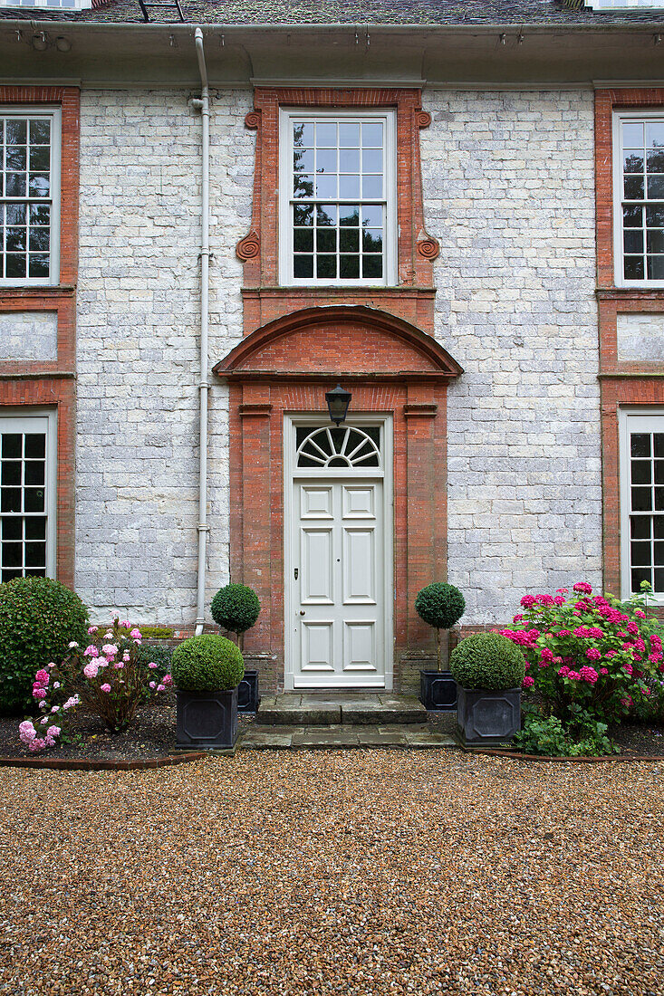 Schotterauffahrt und Eingangstür eines Landhauses aus Stein und Ziegeln in Sussex, England, UK
