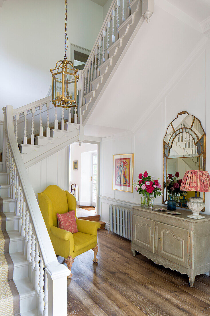 Yellow armchair in staircase hallway of Sussex country house England UK