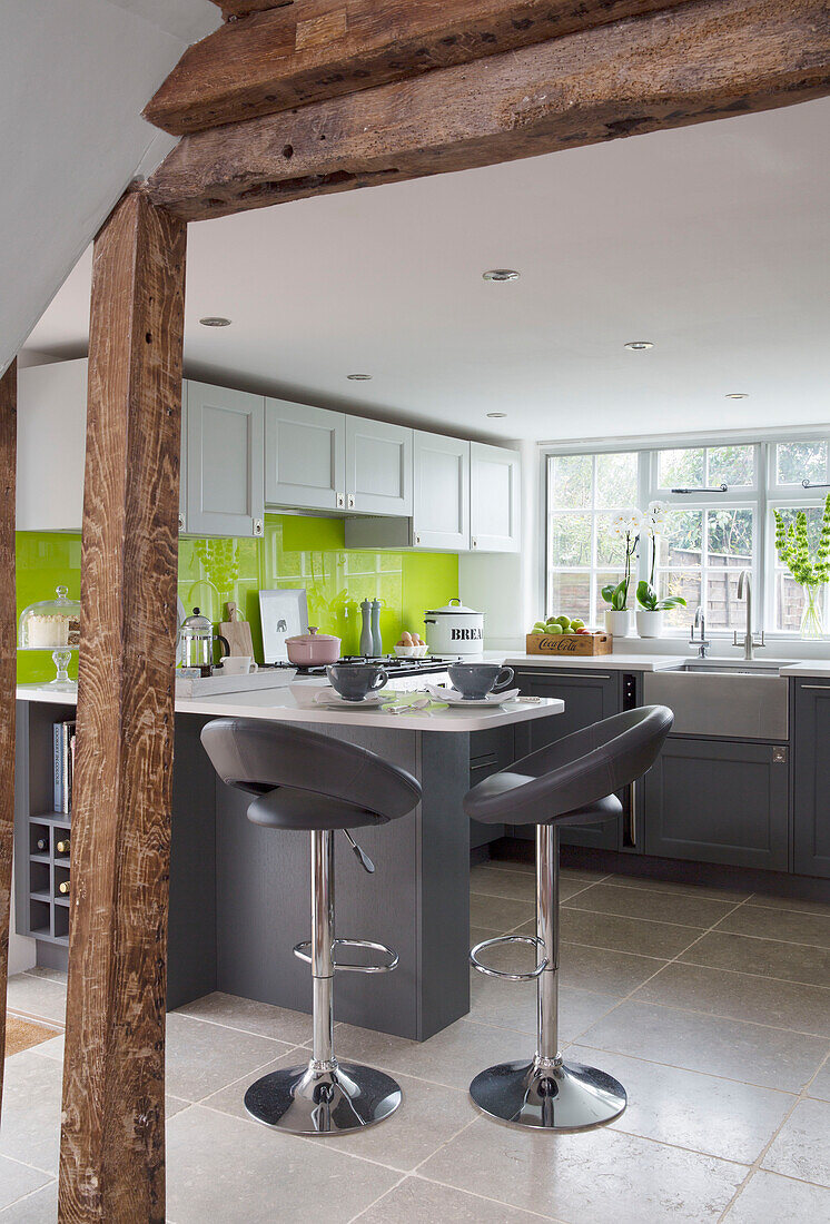 Graue Barhocker in einer modernen Küche mit Holzrahmen in Surrey mit lindgrüner Spritzschutzwand England UK