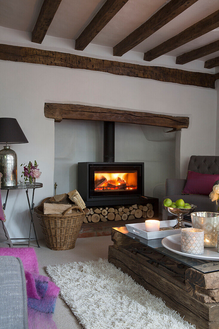 Lit fire and candles with pallet table in beamed Surrey living room England UK