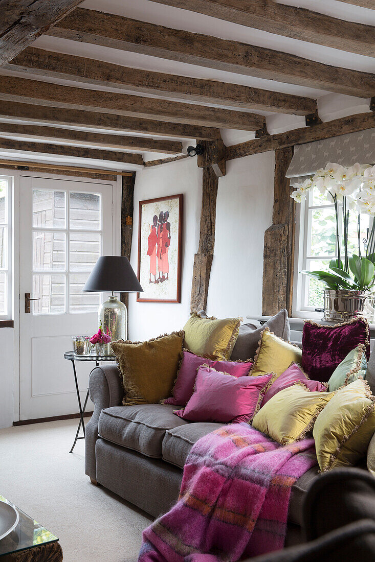Goldfarbene und rosafarbene Kissen auf dem Sofa im Eingangsraum mit Balken in Surrey England UK