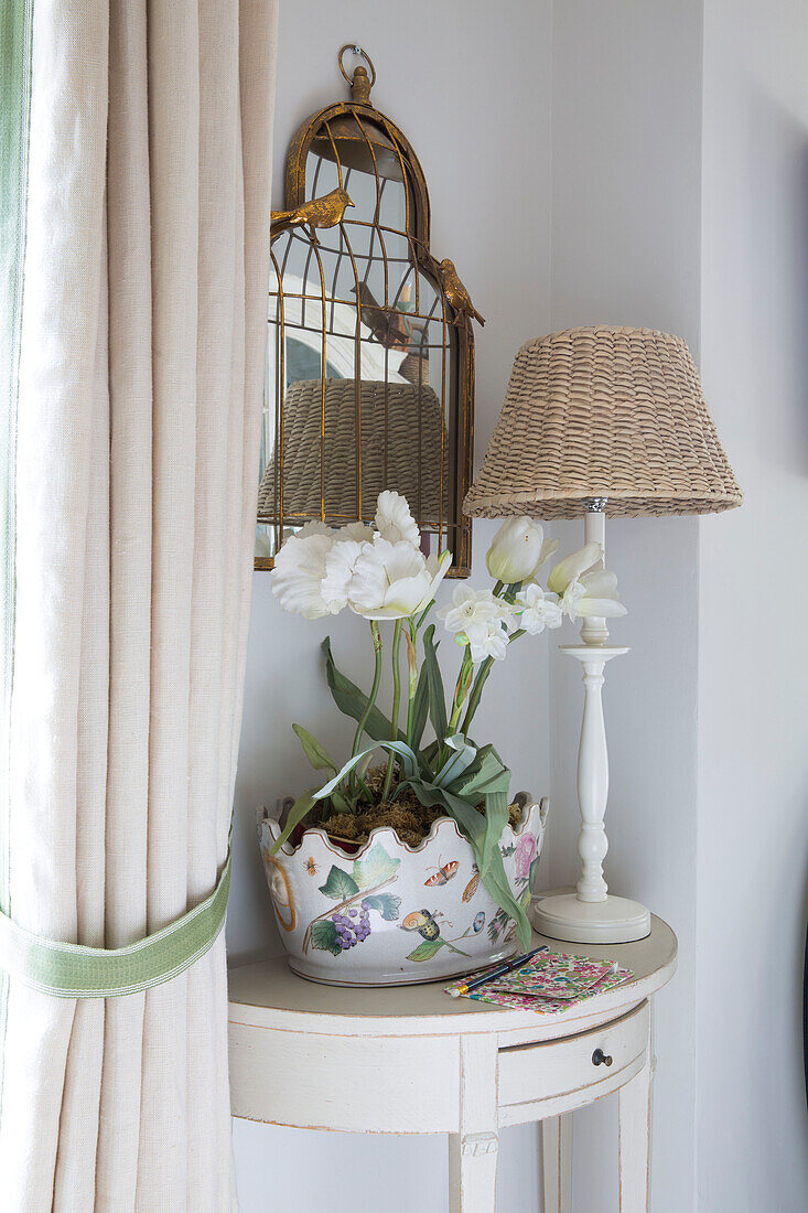 Lampenschirm aus Weidengeflecht und Zimmerpflanze mit Vintage-Spiegel auf einem Demi-Lune-Tisch in einem Haus in Dorset, England, UK