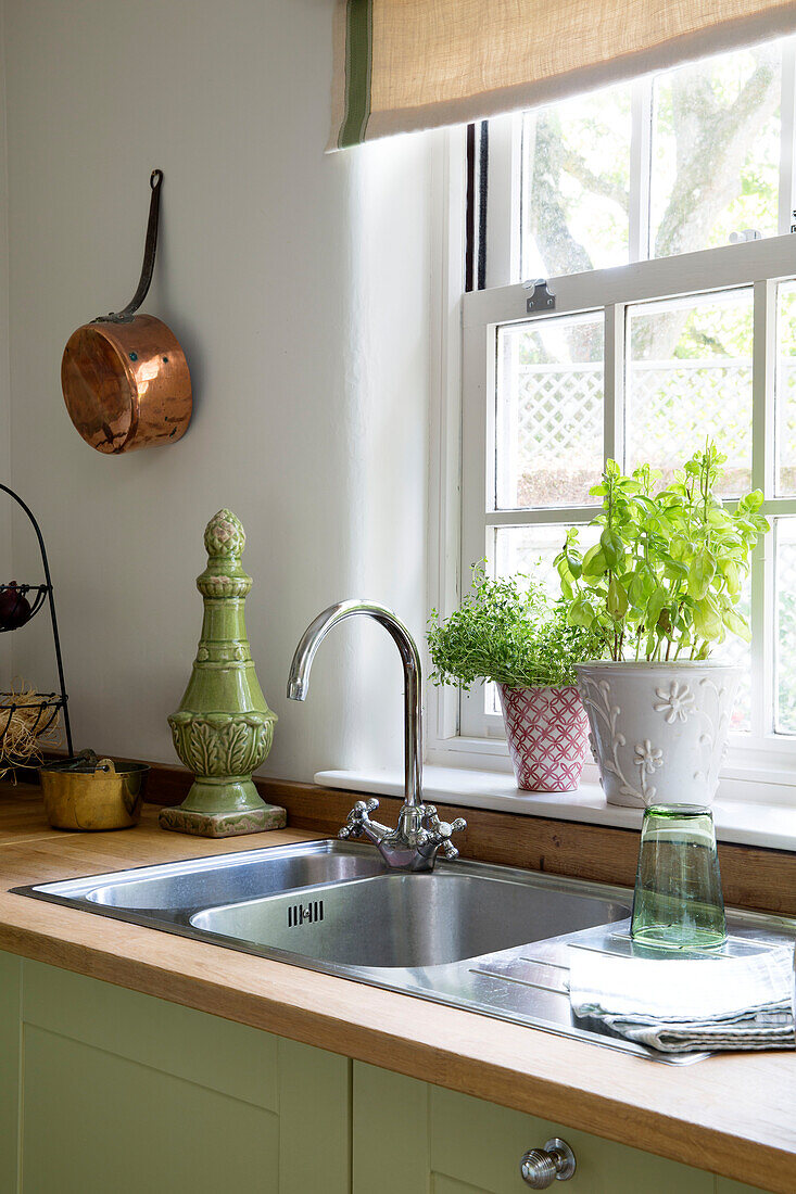 Copper pan next to sink with herbs at windowsill in Dorset kitchen England UK