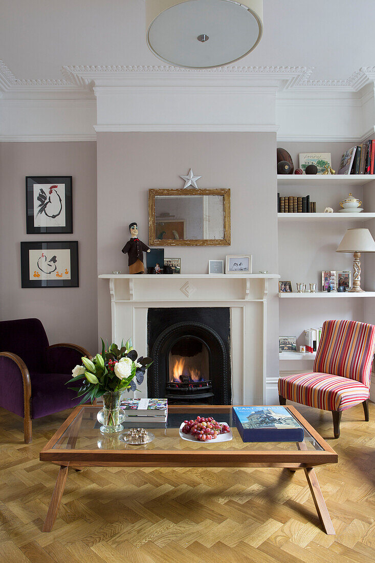 Sessel und Couchtisch mit beleuchtetem Kamin im Wohnzimmer eines viktorianischen Familienhauses in South West London UK
