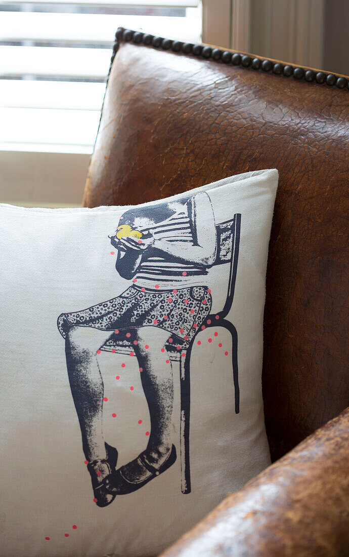 Printed fabric cushion on brown leather armchair in Victorian family home South West London UK
