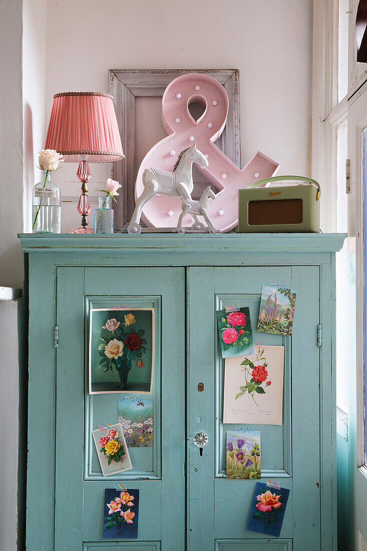 Pink lamp and ampersand on blue cupboard with botanical postcards in Norfolk home England UK