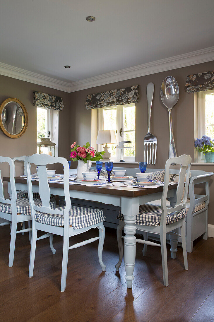 Bemalte Esszimmerstühle mit karierten Sitzbezügen am Tisch mit großem Löffel und Gabel in einem Landhaus in Wokingham, Berkshire, Großbritannien