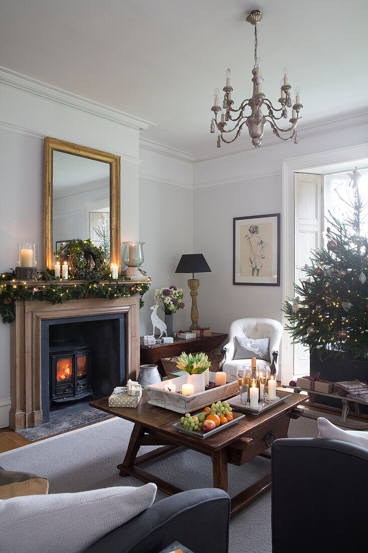 Obst und Kerzen vor einem beleuchteten Holzofen und einem Weihnachtsbaum in einem Haus in Surrey, England