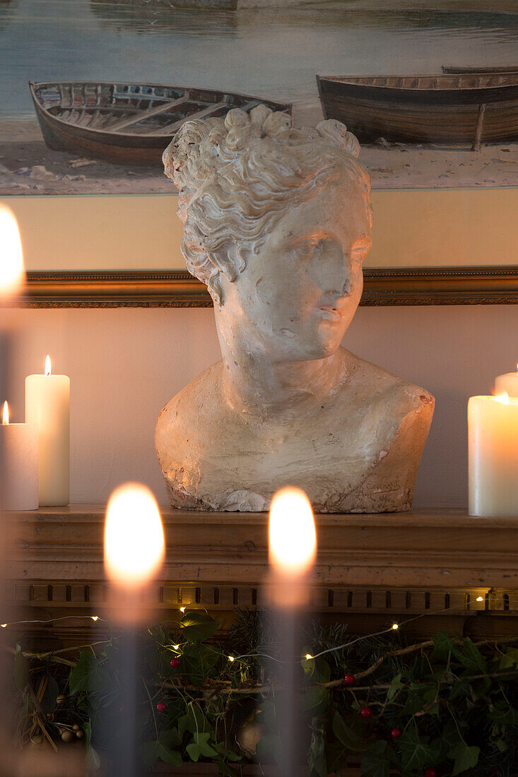 Büste auf hölzernem Kaminsims mit brennenden Kerzen in einem Haus in Surrey, England, UK