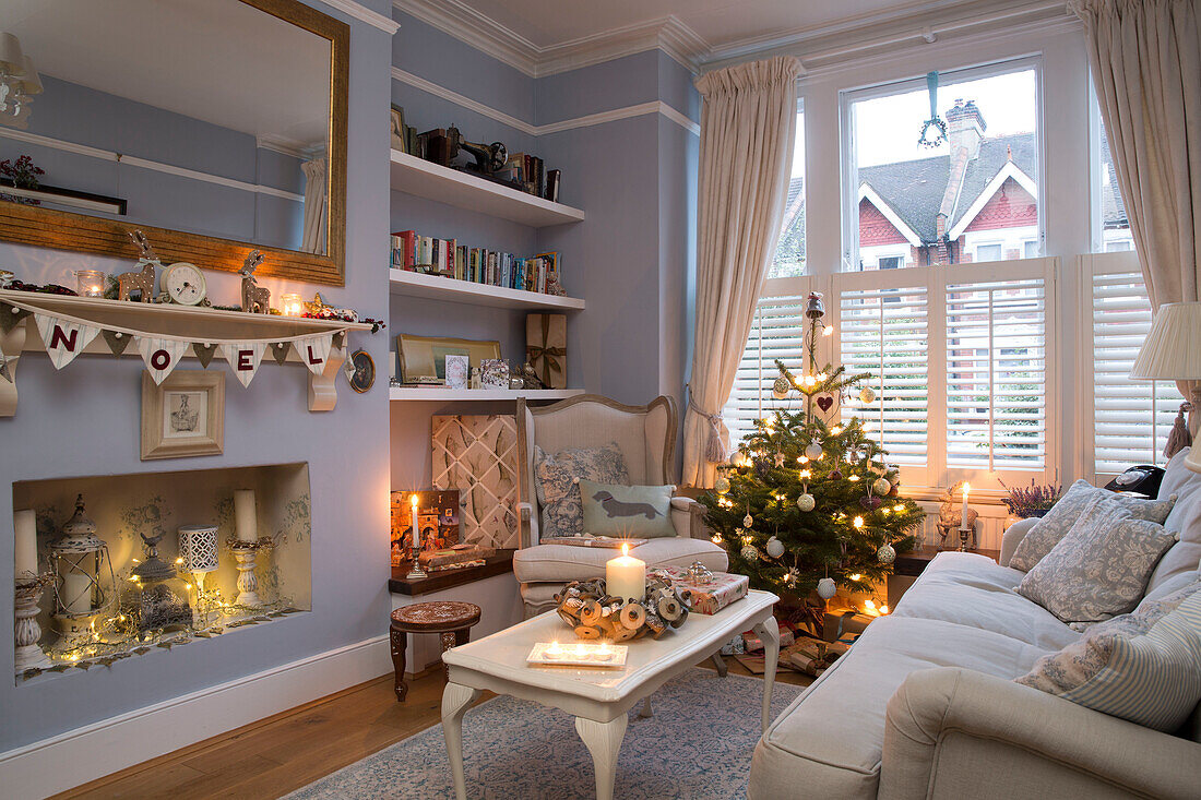 Beleuchtete Kerzen und Weihnachtsbaum mit Girlande im Wohnzimmer eines Londoner Hauses, England UK