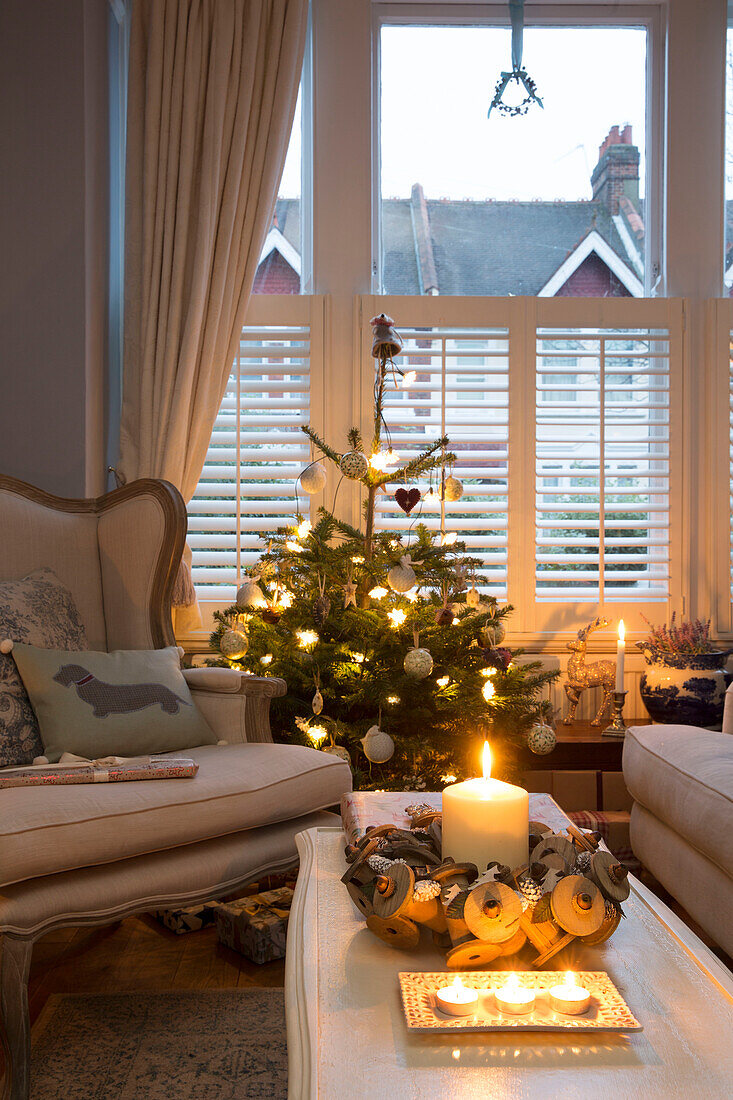 Beleuchtete Kerze auf einem Couchtisch mit Weihnachtsbaum am Fenster in einem Haus in London, England UK