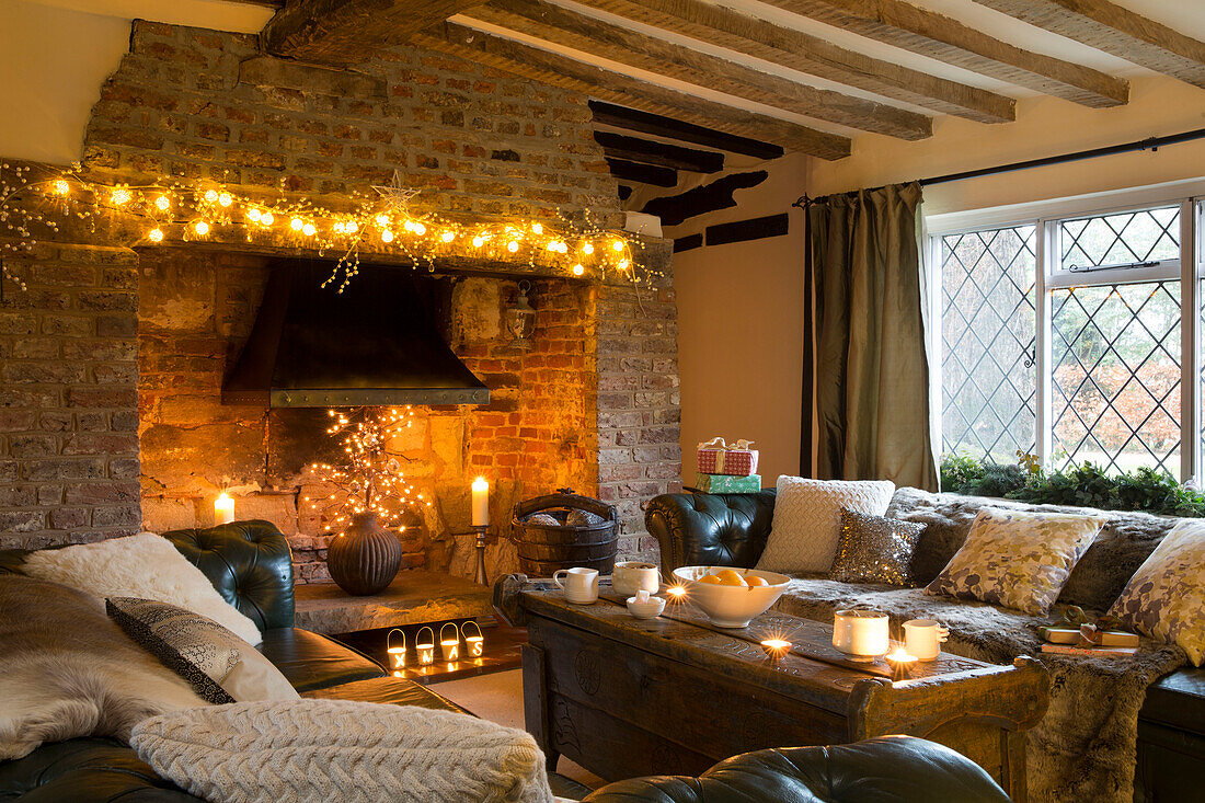 Lit fairylights on brick fireplace with green Chesterfield in Kent living room England UK