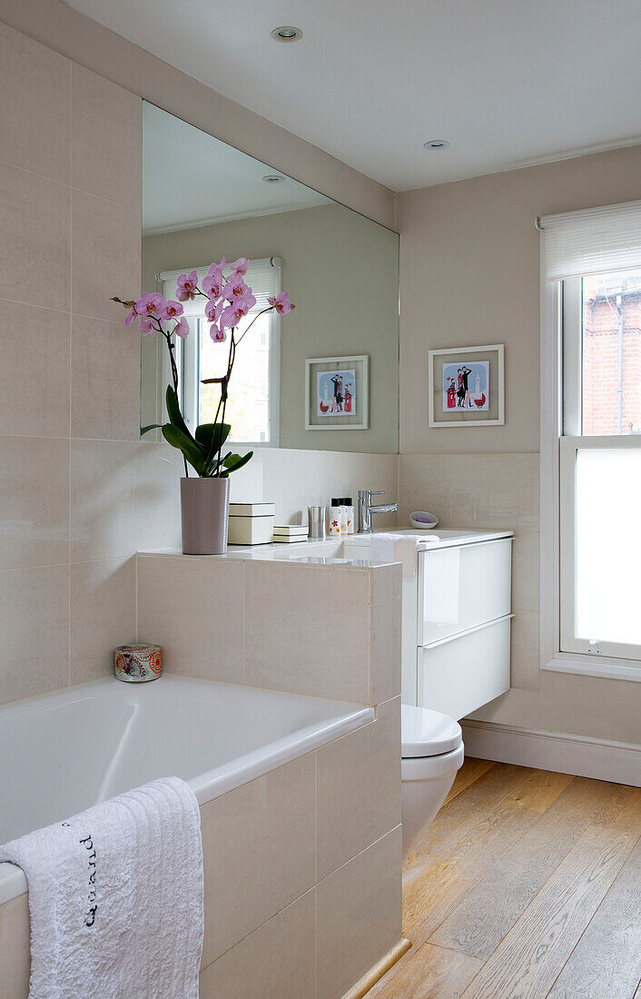 Orchidee im weißen Badezimmer mit großem Spiegel und Holzboden in einem Einfamilienhaus im Südwesten Londons UK