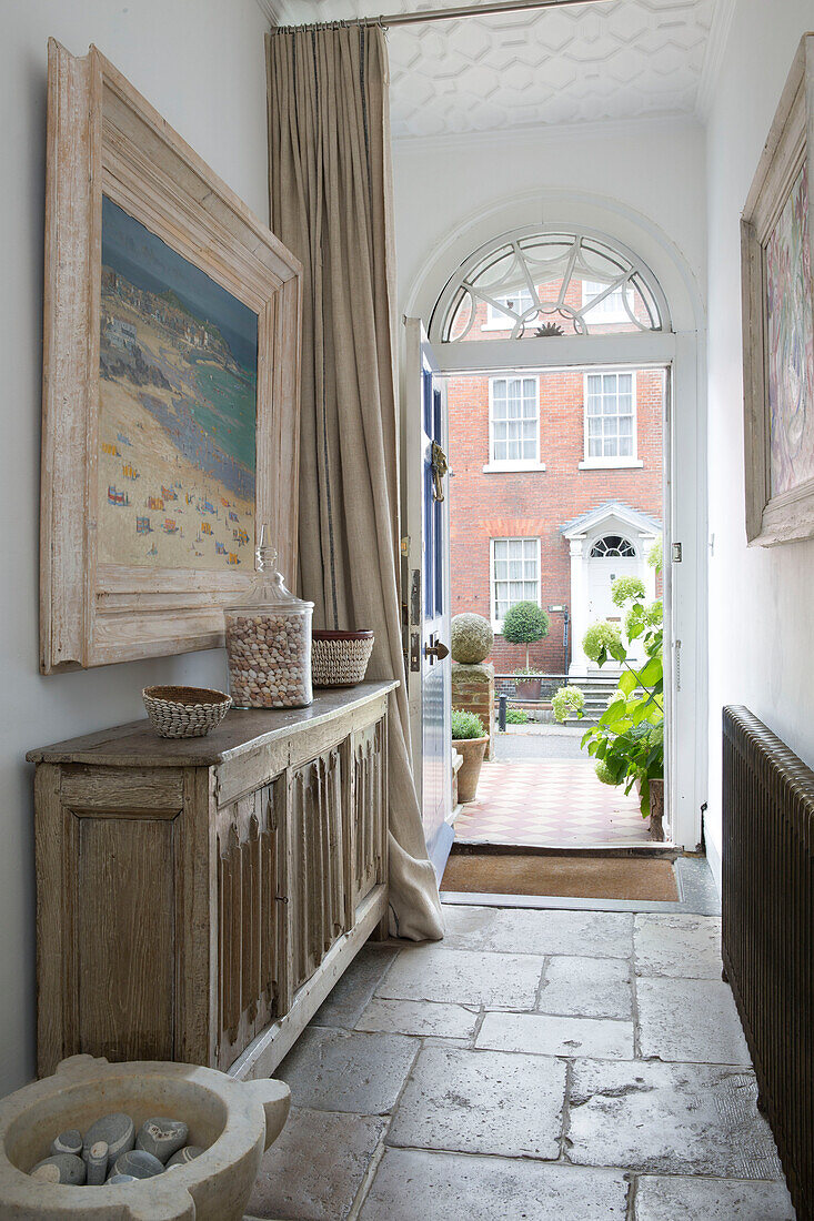 Großes Kunstwerk über einer Konsole in einem mit Fliesen ausgelegten Flur mit Blick durch die Eingangstür eines Hauses in Arundel, West Sussex, England UK