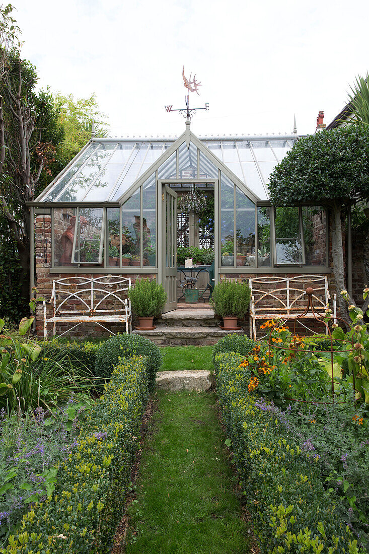 Gewächshaus mit Wetterfahne und rostigen Bänken im Garten von Arundel, West Sussex, England, UK
