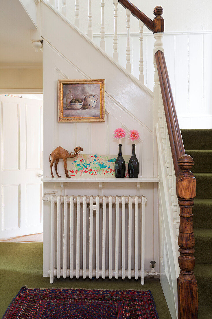 Wooden banister in hallway with single stem flowers and camel on radiator shelf in Berkshire home England UK