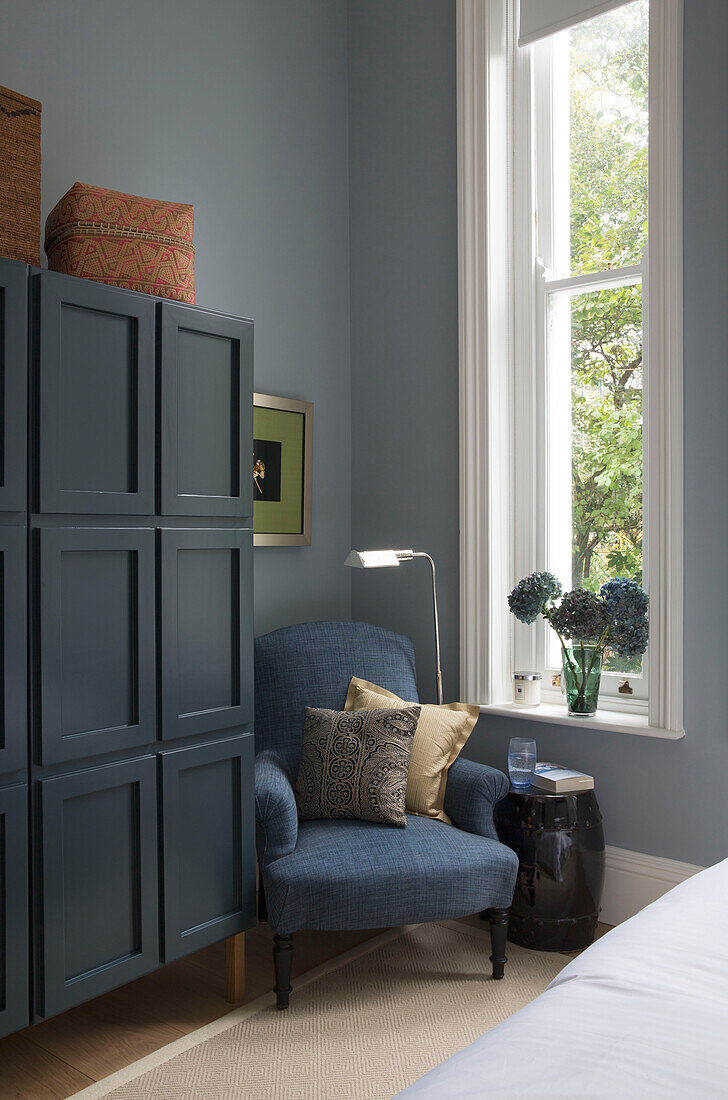 Blauer Sessel und tealfarbener Schrank am Fenster im Schlafzimmer eines Londoner Stadthauses UK