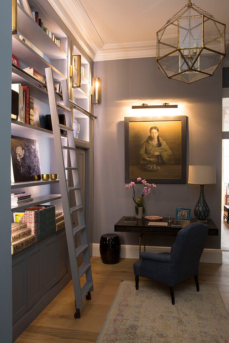 Schreibtisch und Stuhl mit beleuchteter Bilderleuchte und Bücherregal im Arbeitszimmer eines Londoner Stadthauses UK