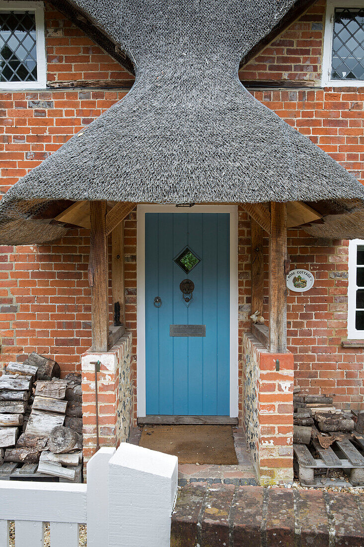 Thatched porch entrance with firewood of Grade II listed cottage Hampshire England UK