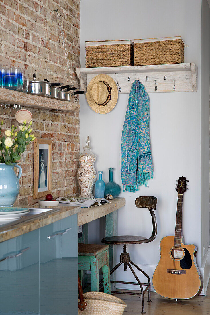 Gitarre und Schreibtisch mit Töpfen auf einem Regal in einer Küche aus Backsteinen in einem Strandhaus in Sussex (England)