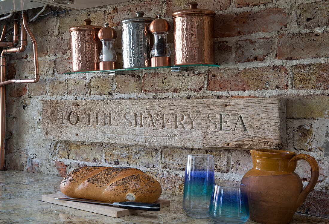 Carved plaque with tins and bread in exposed stone kitchen of Sussex beach house England UK