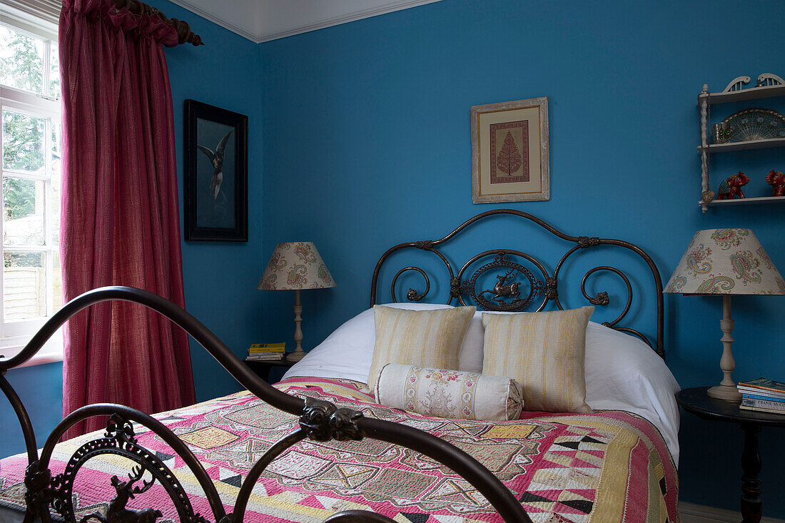 Patchwork-Bezug auf einem Bett mit Metallrahmen in einem blauen Schlafzimmer in einem Haus in Sussex (England)