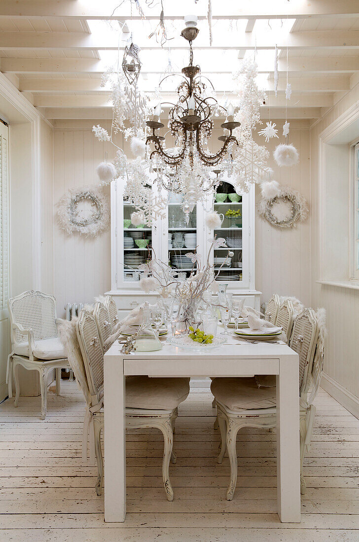 Chandelier and Christmas decorations hang above white dining table in South London England UK
