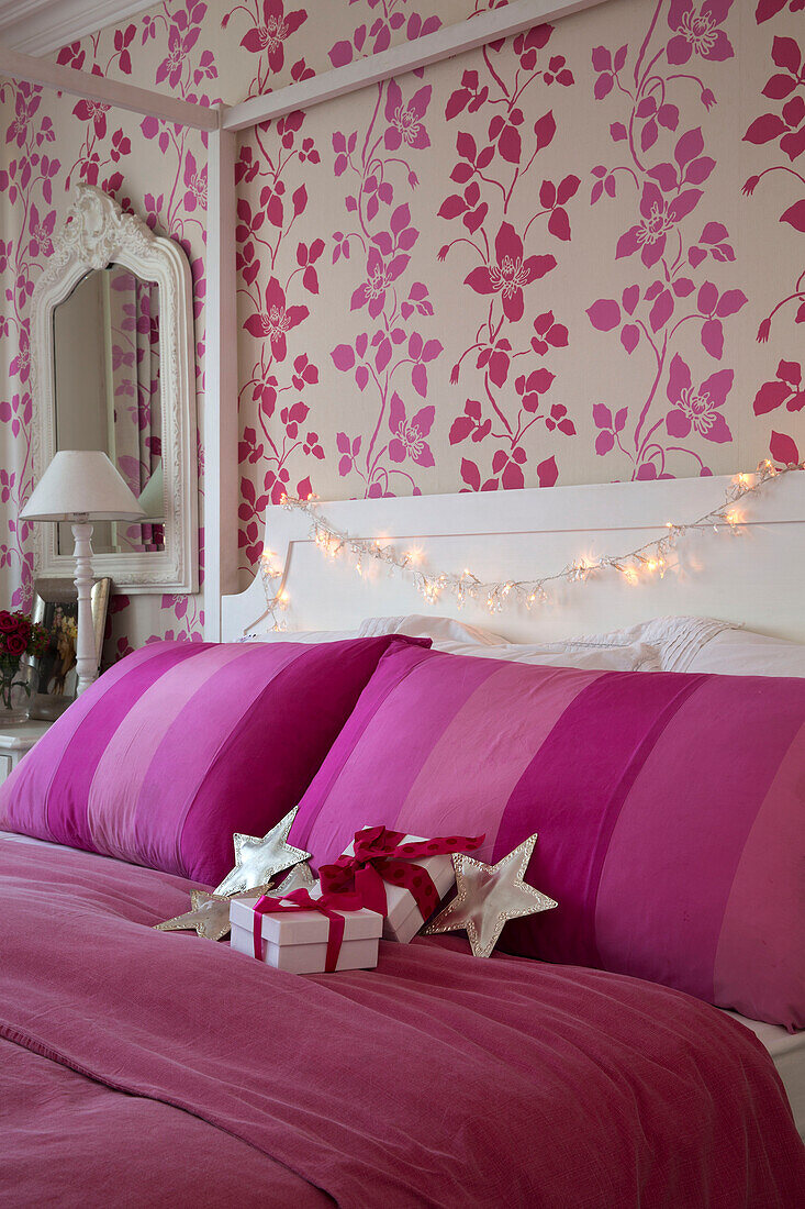 Christmas presents on bright pink cover on four poster bed with floral paper in South London home England UK