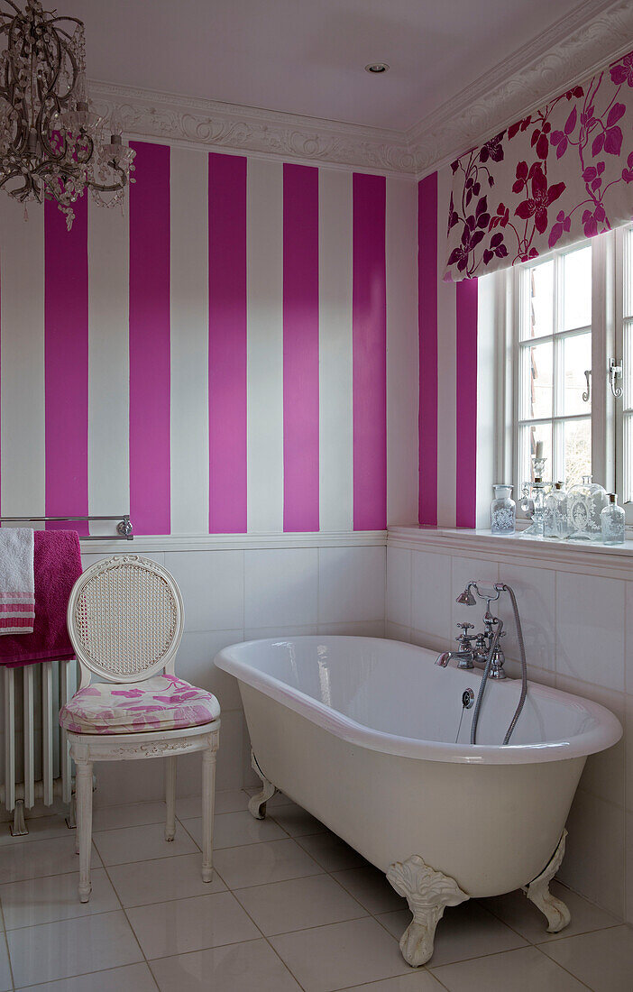 Freistehende Badewanne unter dem Fenster mit rosa gestreifter Tapete in einem Badezimmer in Südlondon, England UK