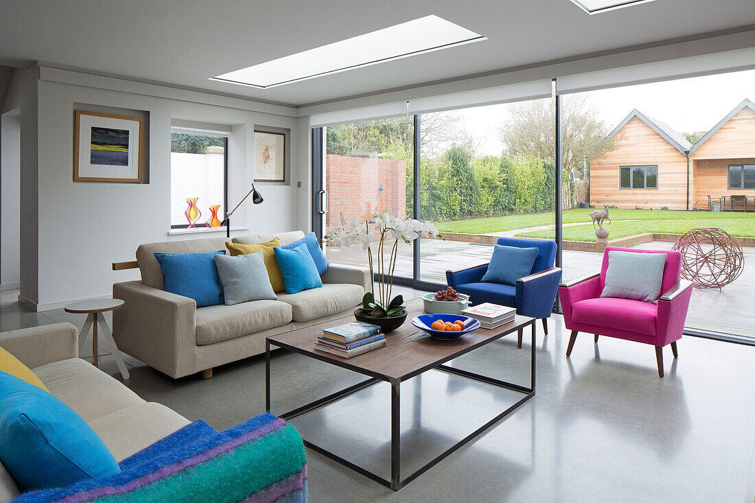 Rosa und blaue Sessel mit Sofa und Couchtisch unter Oberlichtern in einem modernisierten viktorianischen Cottage in Sussex, England, UK