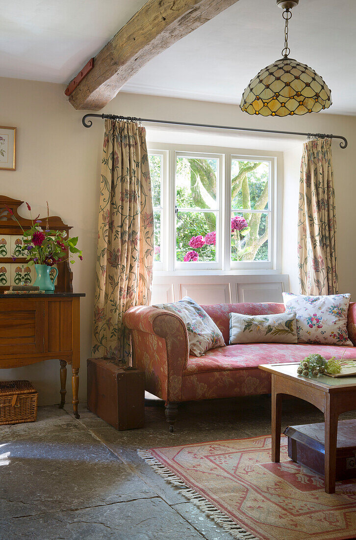 Vintage-Sofa unter sonnenbeschienenem Fenster mit Originalfußboden im Wohnzimmer eines Landhauses in Somerset, England, 19
