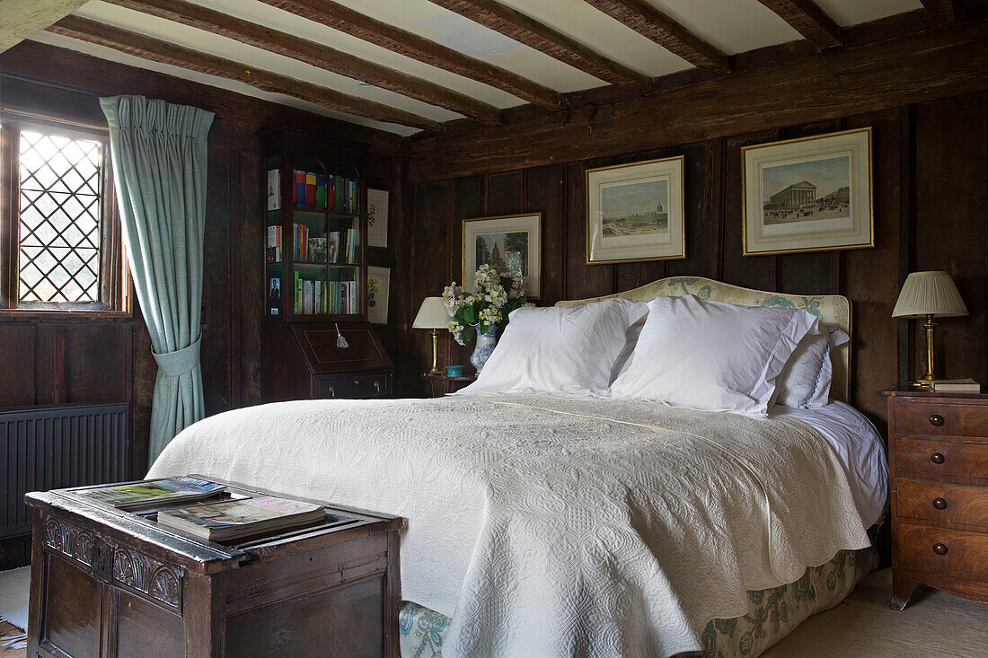 Antique wooden blanket box at foot of double bed with white cover in panelled Kent farmhouse UK