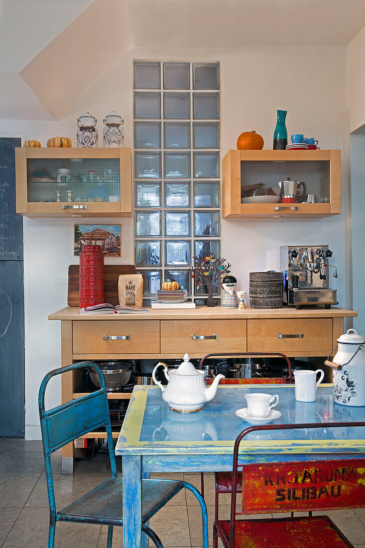 Glass bricks and wall mounted shelves with vintage metal chairs in London kitchen England UK
