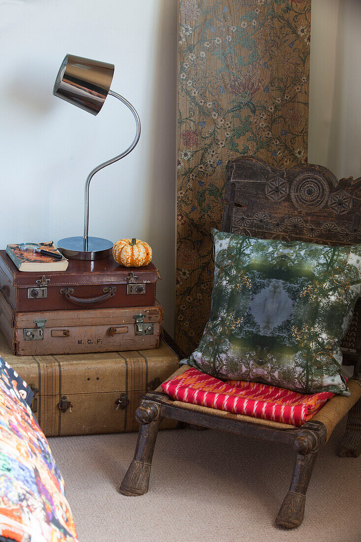 Low carved chair with vintage suitcases at bedside in London home England UK