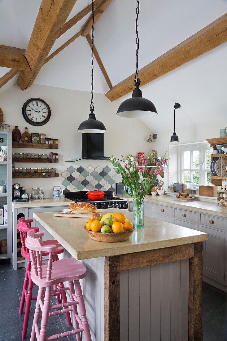 Fruit bowl on kitchen island with pink painted barstools in beamed Sussex kitchen with spice rack England UK