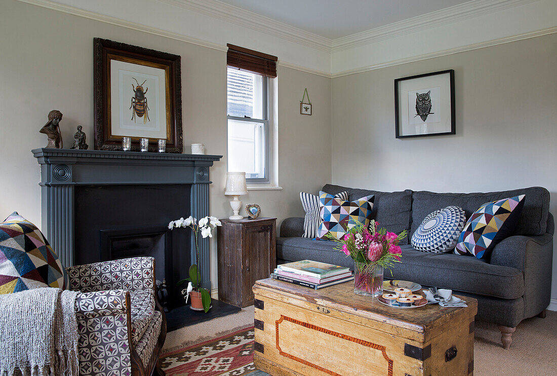 Grey sofa and fireplace with wooden chest and upholstered armchair in Sussex living room England UK
