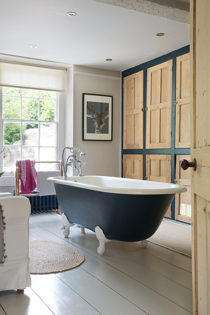 Dunkelblaue freistehende Badewanne mit holzgetäfelten Schränken in einem Haus in Gloucestershire, England, UK