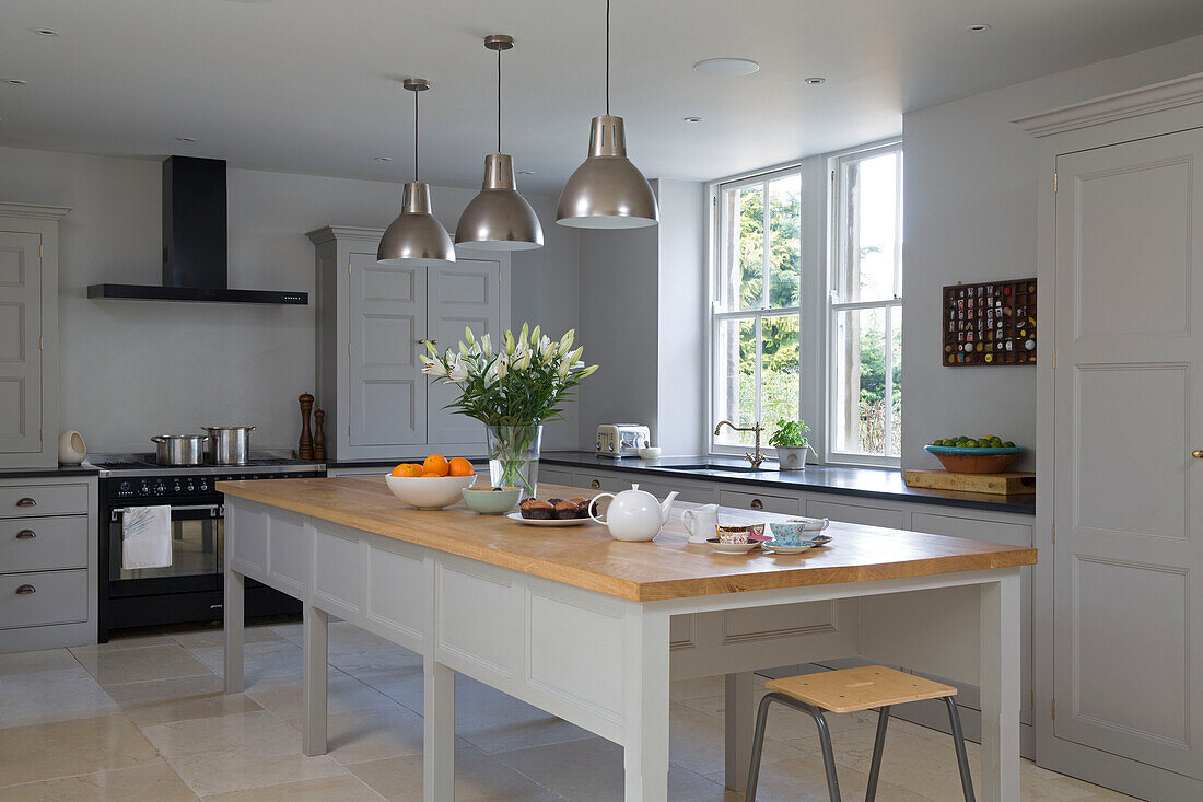 Brushed stainless steel pendant lights above long wooden table in Gloucestershire home England UK
