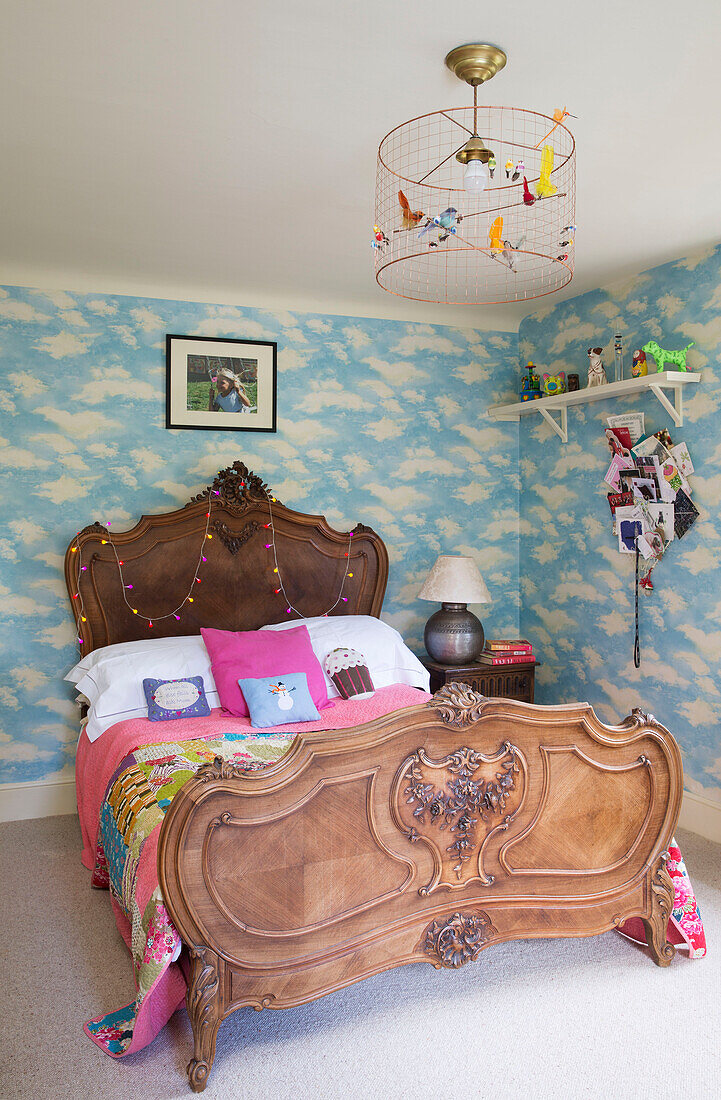 Carved wooden bed with cloud patterned wallpaper in Gloucestershire home England UK