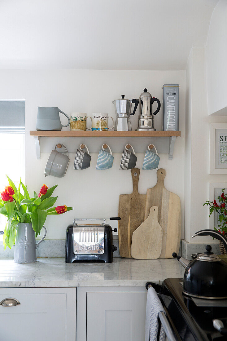 Tassen hängen auf Küchenregal über Schneidebrettern und Toaster in Worcestershire home England UK